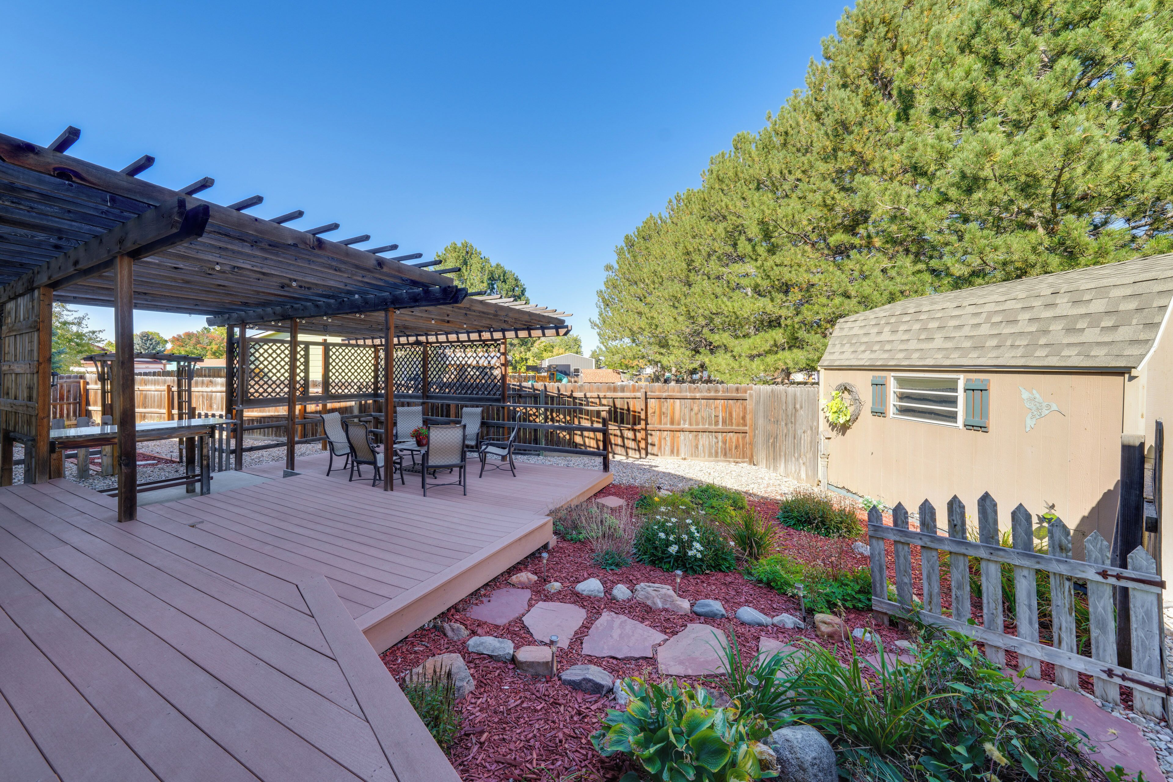 A wooden deck with outdoor furniture, a pergola, and a garden area with rocks and plants.