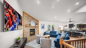 Un salón amplio con chimenea, televisor grande y zona de comedor con cocina al fondo.