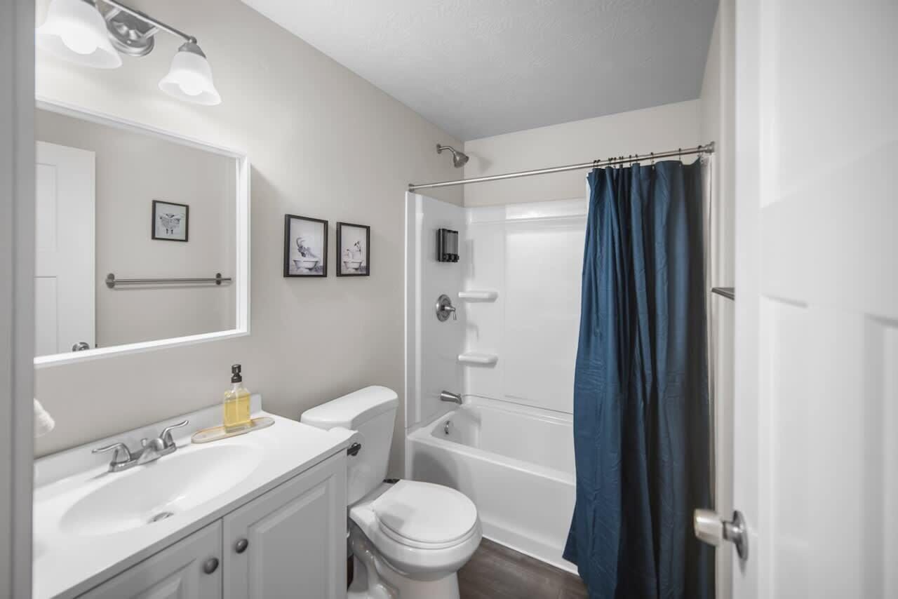 A bathroom with a white sink, toilet, and bathtub. There are framed pictures on the wall and a towel rack above the sink.