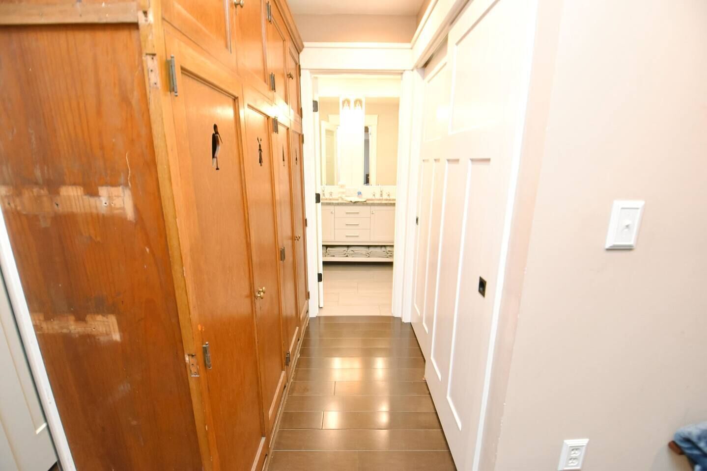 A hallway with wooden doors, a tiled floor, and a view into a bathroom with a mirror and sink.