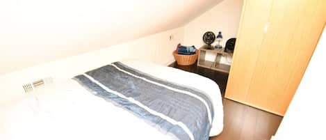 A bedroom with a bed, a wooden wardrobe, a small table with a lamp, and a wall clock.