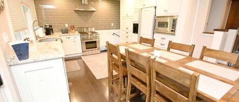 Cozinha moderna com armários brancos, mesa de jantar de madeira e eletrodomésticos de aço inoxidável.