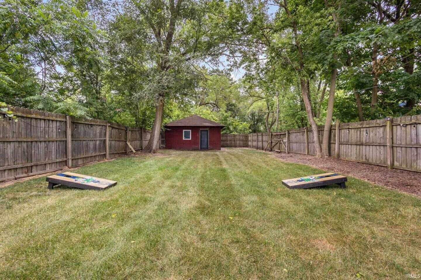 A backyard with a wooden fence, a small shed, and two shuffleboard tables.