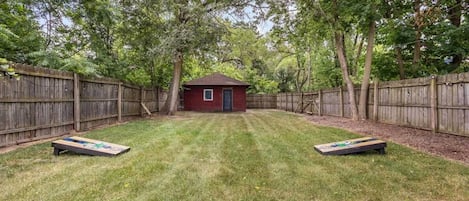 A backyard with a wooden fence, a small shed, and two shuffleboard tables.