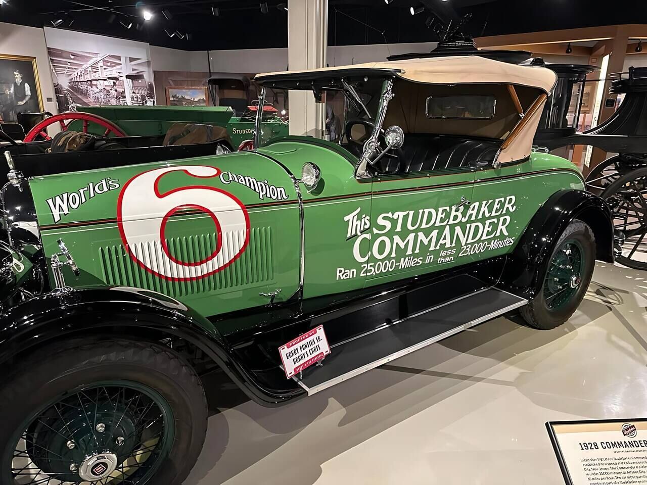A vintage green car with 'World's Champion' and 'The Studebaker Commander' text, displayed in a museum setting.
