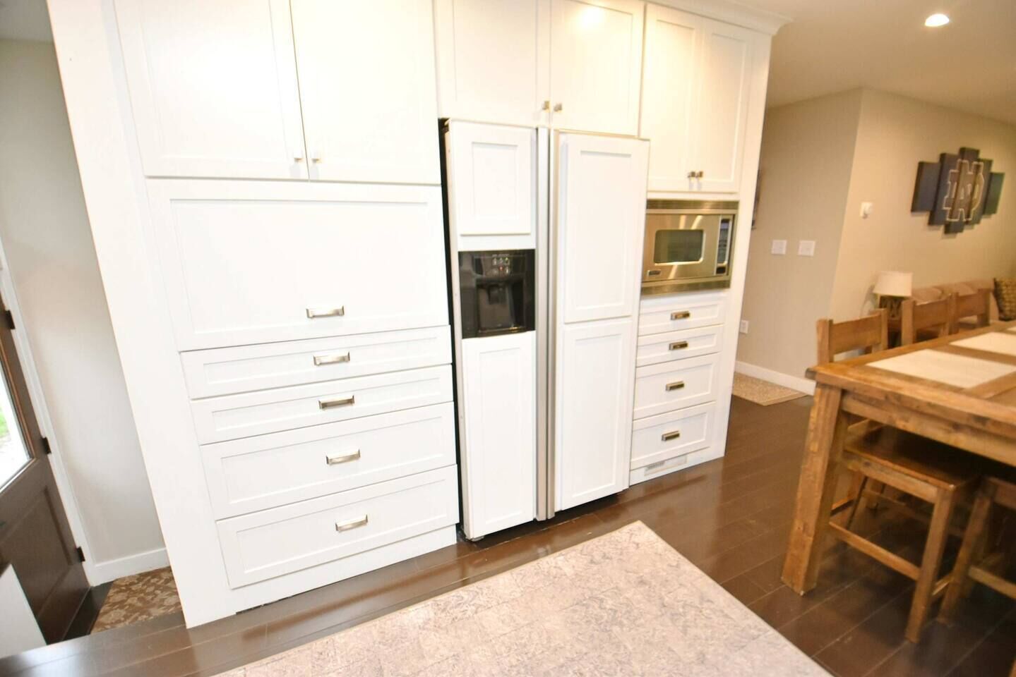 Una cocina con muebles blancos, un refrigerador, un horno y una mesa de comedor con sillas.