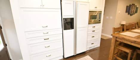 Una cocina con muebles blancos, un refrigerador, un horno y una mesa de comedor con sillas.