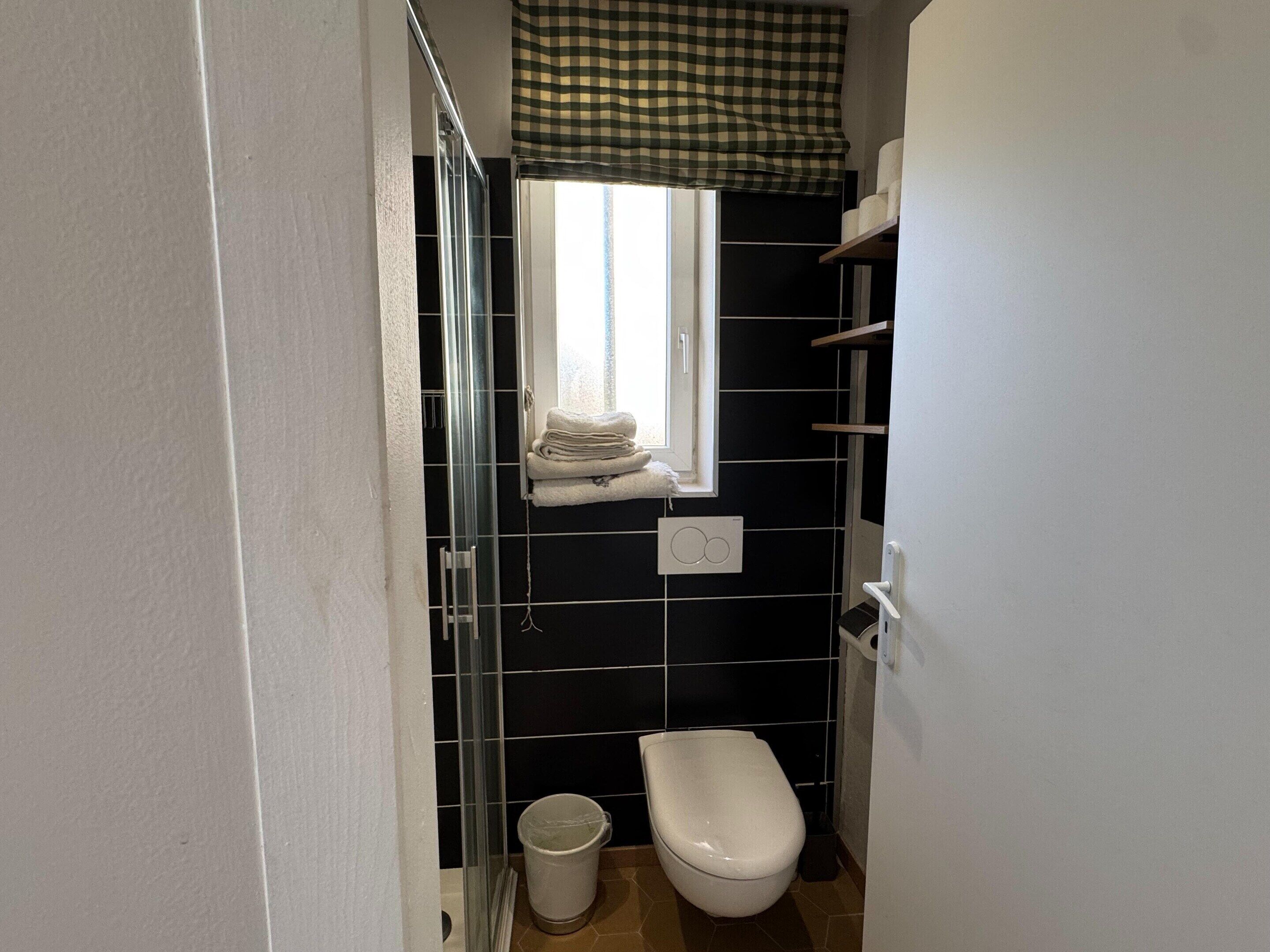 A small bathroom with a toilet, a window with a checkered curtain, and a towel rack.