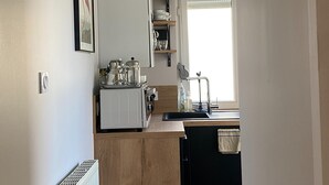 A compact kitchen with a built-in oven, a sink, and a window with blinds. - Charming Stay in the Heart of Vittel (Vittel)