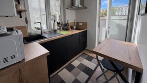 A compact kitchen with a sink, countertop, and a dining area with a table and chair. - Charming Stay in the Heart of Vittel (Vittel)