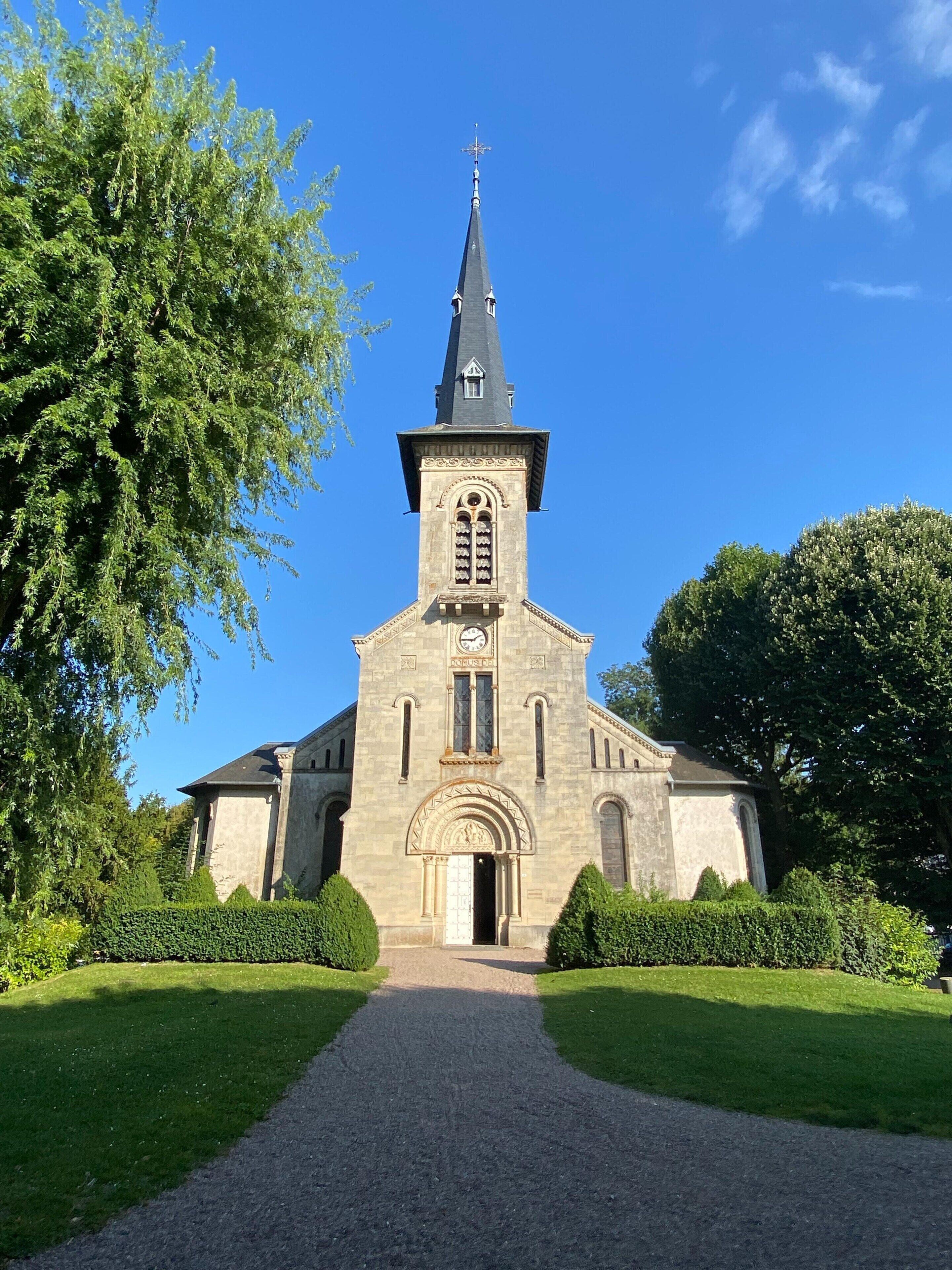 A church with a tall steeple, a central entrance, and a gravel pathway leading to it.