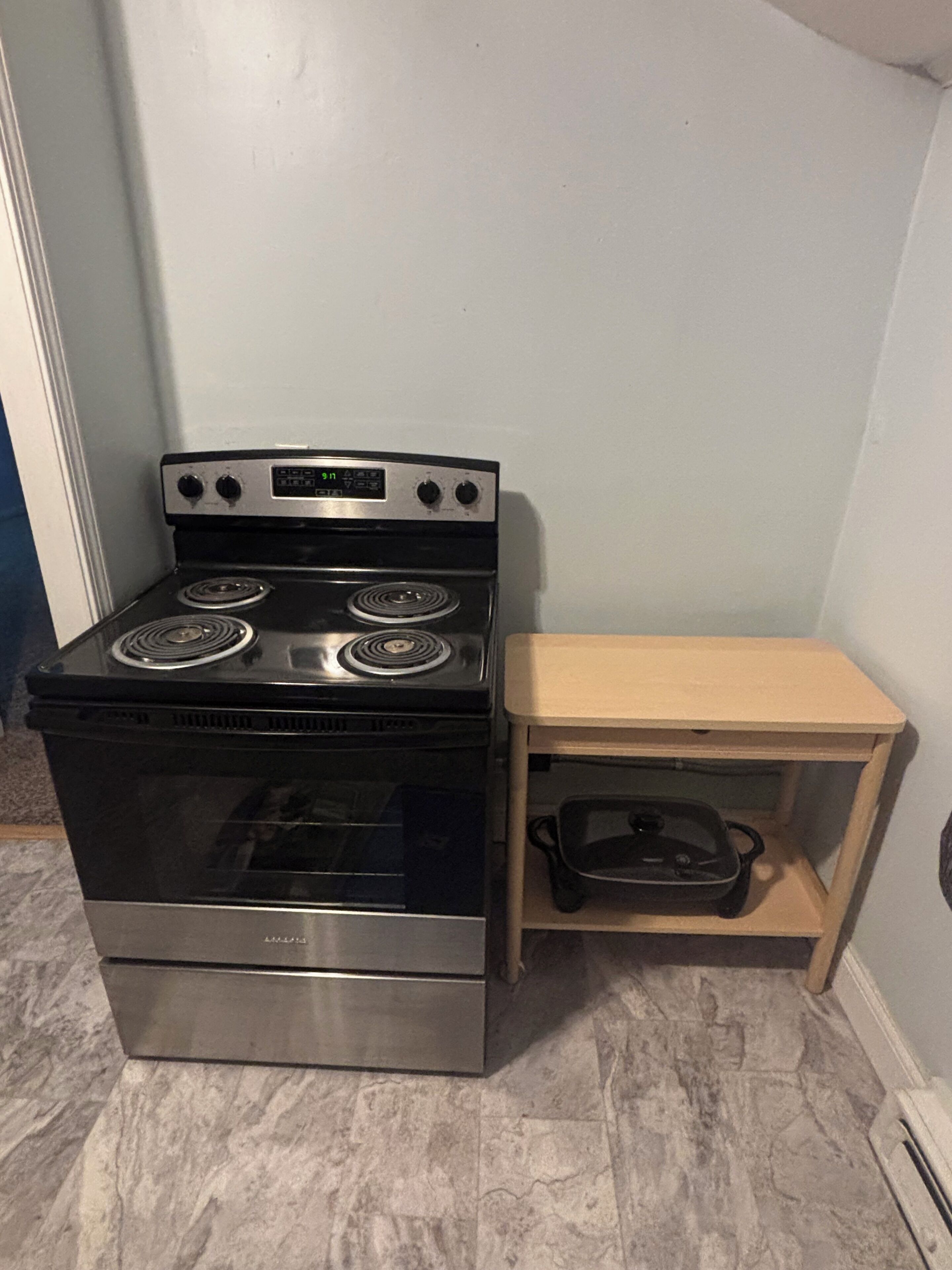 A compact kitchen with a black stove, a wooden shelf, and a pot.