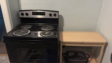 A compact kitchen with a black stove, a wooden shelf, and a pot.
