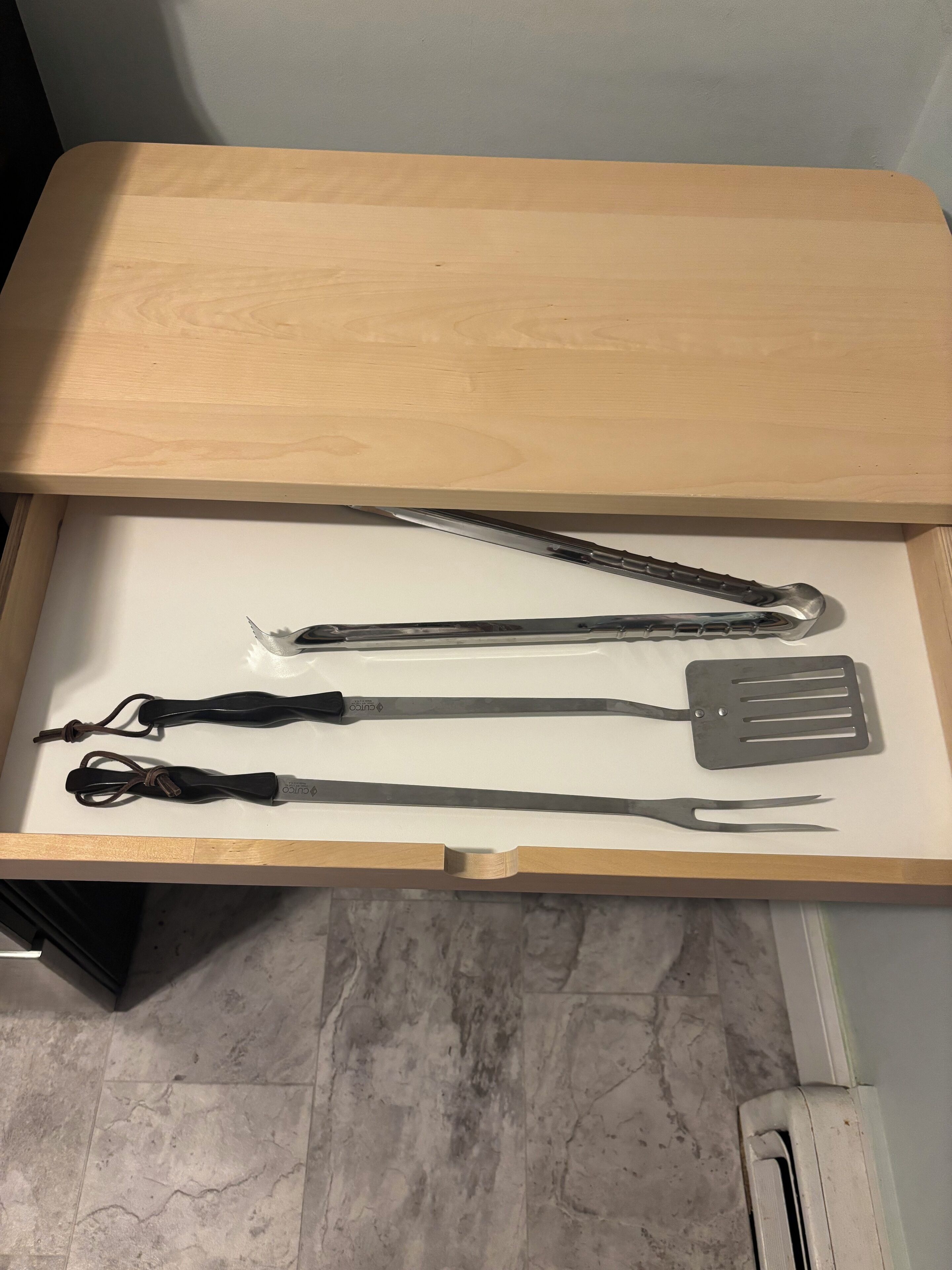 A drawer with kitchen utensils including a spatula, tongs, and a pair of scissors.