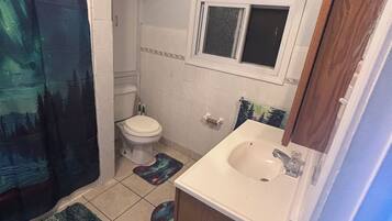 A small bathroom with a toilet, sink, and window. There are two rugs on the floor.