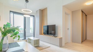 A modern living room with a flat-screen TV, a dining area with a table and chairs, and a large window providing natural light. - Stylish 1BR & 1LR Apartment | Cozy City View (Bratislava)