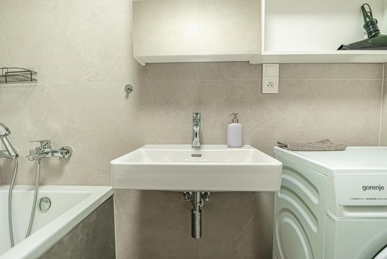 Ein Badezimmer mit einem weißen Waschbecken, einer Dusche und einer Waschmaschine.