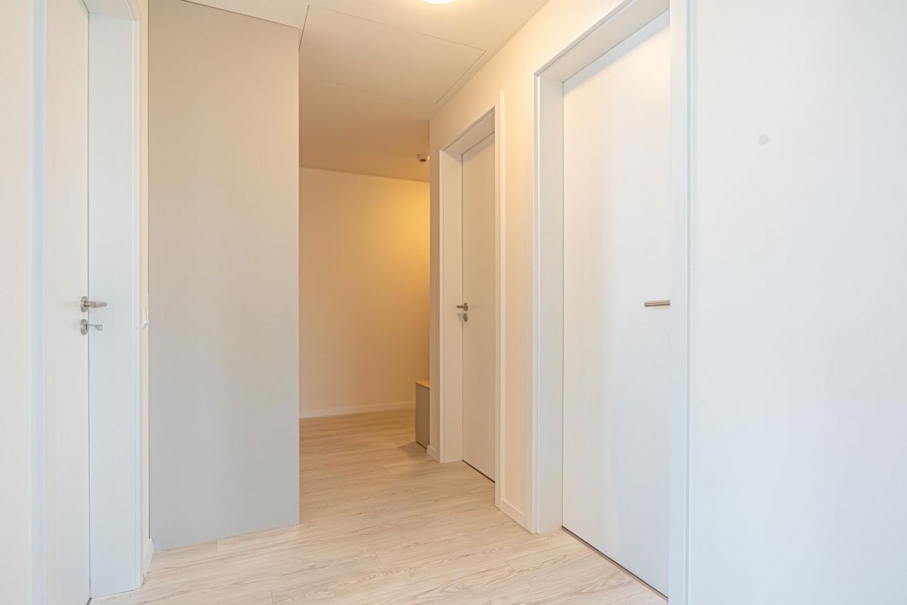 A hallway with white doors and a light wooden floor.