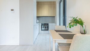 A modern kitchen with wooden cabinets, a built-in oven, and a dining area with a table and chairs. - Stylish 1BR & 1LR Apartment | Cozy City View (Bratislava)