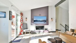 Un salon moderne avec un téléviseur à écran plat fixé au mur, un canapé, une table basse et une cheminée.