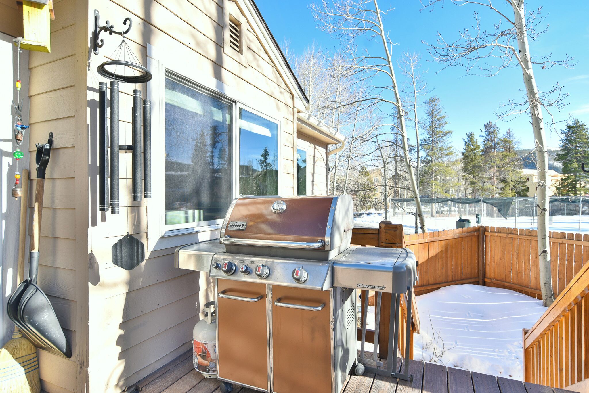 A wooden deck with a barbecue grill, a wooden fence, and a window overlooking a snowy landscape.