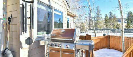 A wooden deck with a barbecue grill, a wooden fence, and a window overlooking a snowy landscape.