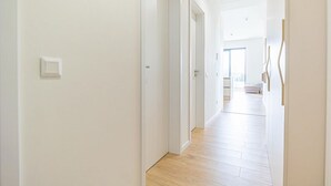 Un pasillo con paredes blancas y suelo de madera que conduce a una habitación con un ventanal grande.