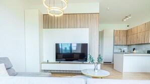 Una sala de estar moderna con un televisor de pantalla plana, un sofá, una mesa de centro y una zona de cocina con armarios de madera.