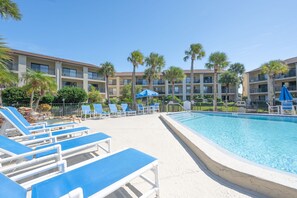 A pool area with blue lounge chairs and umbrellas, surrounded by palm trees and a multi-story building. - 3BR Poolside Condo Near Beach (St. Augustine)