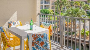Een balkon met een witte tafel, gele stoelen en een groene fles.