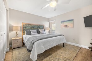 A bedroom with a bed, nightstands, a ceiling fan, a painting, and a TV. - 3BR Poolside Condo Near Beach (St. Augustine)