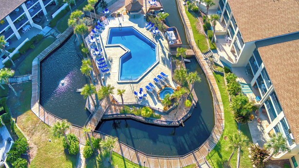 Luchtbeeld van een resort met een centraal gelegen zwembad, omringd door ligbedden en palmbomen.