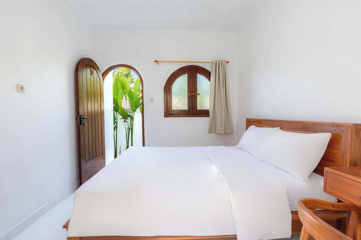 Un dormitorio con una cama de madera, un ventanal con cortina y una puerta con una planta afuera.