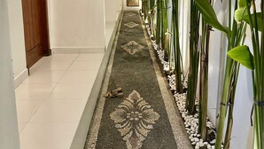 A corridor with a patterned carpet, a wooden door, and tall plants along the walls. - Casa Feliz Guest House (Bangli)