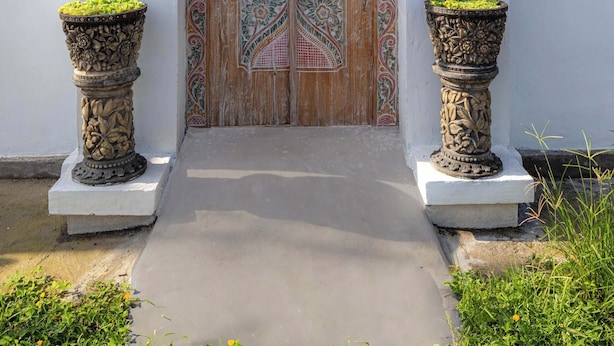 A traditional wooden door with intricate carvings, flanked by two large planters with green plants, and a sign indicating the guesthouse number 12. - Casa Feliz Guest House (Bangli)