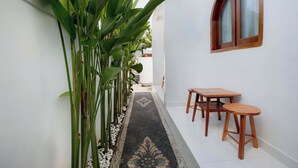 A narrow corridor with a patterned floor, a wooden bench, and a window with a wooden frame. - Casa Feliz Guest House (Bangli)