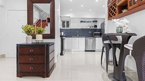 A modern kitchen with white cabinets, a dark wooden dresser, and a dining area with wicker chairs. - NOK Classy 3BR Apartment in Punta Cana Village (Punta Cana)