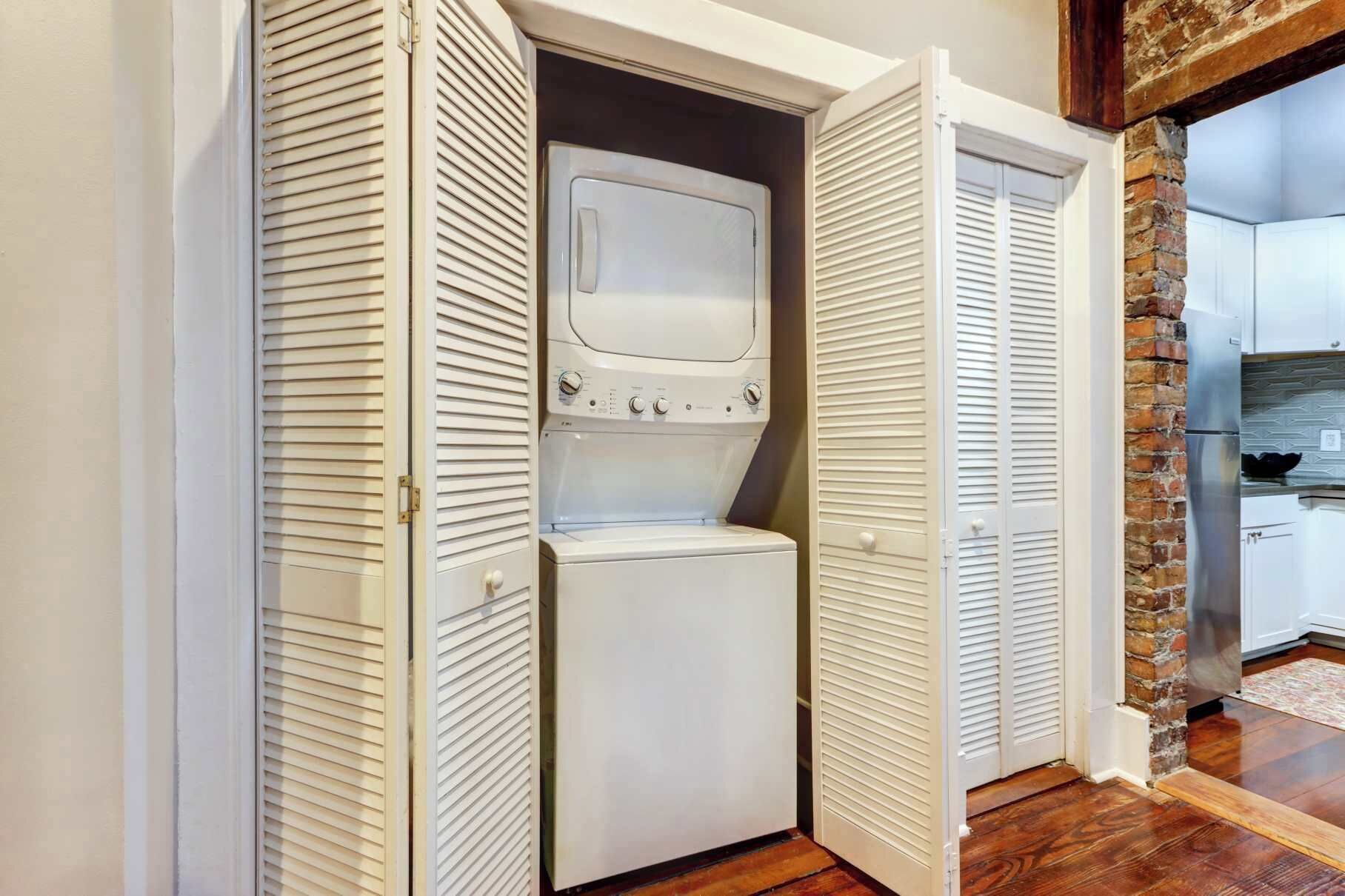 A laundry room with a front-loading washer and dryer, a brick accent wall, and a wooden floor.