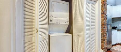 A laundry room with a front-loading washer and dryer, a brick accent wall, and a wooden floor.
