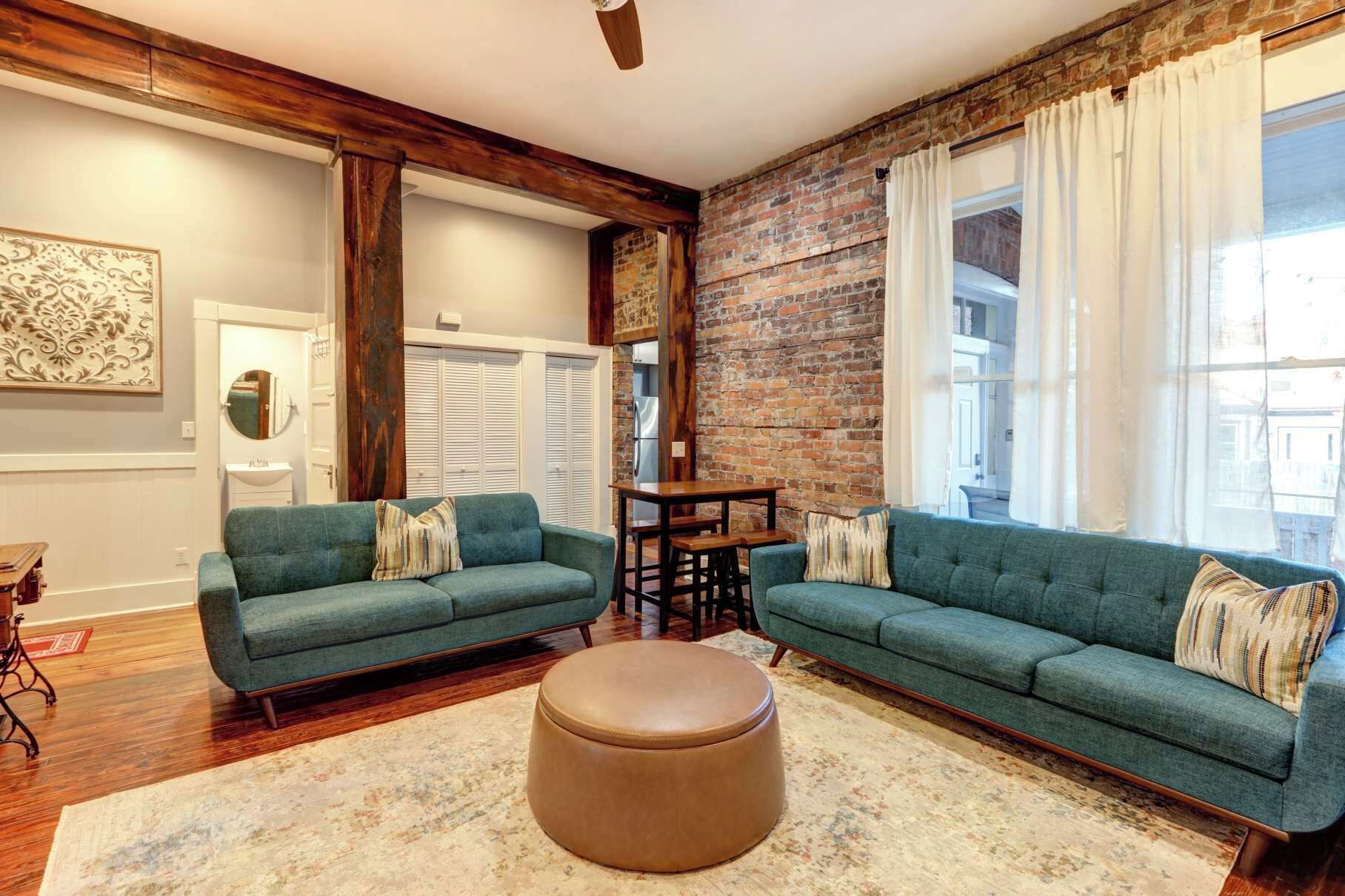 Un salón con dos sofás verdes, una mesa de centro de madera y una pared de ladrillo.