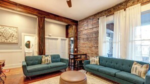 Un salón con dos sofás verdes, una mesa de centro de madera y una pared de ladrillo.