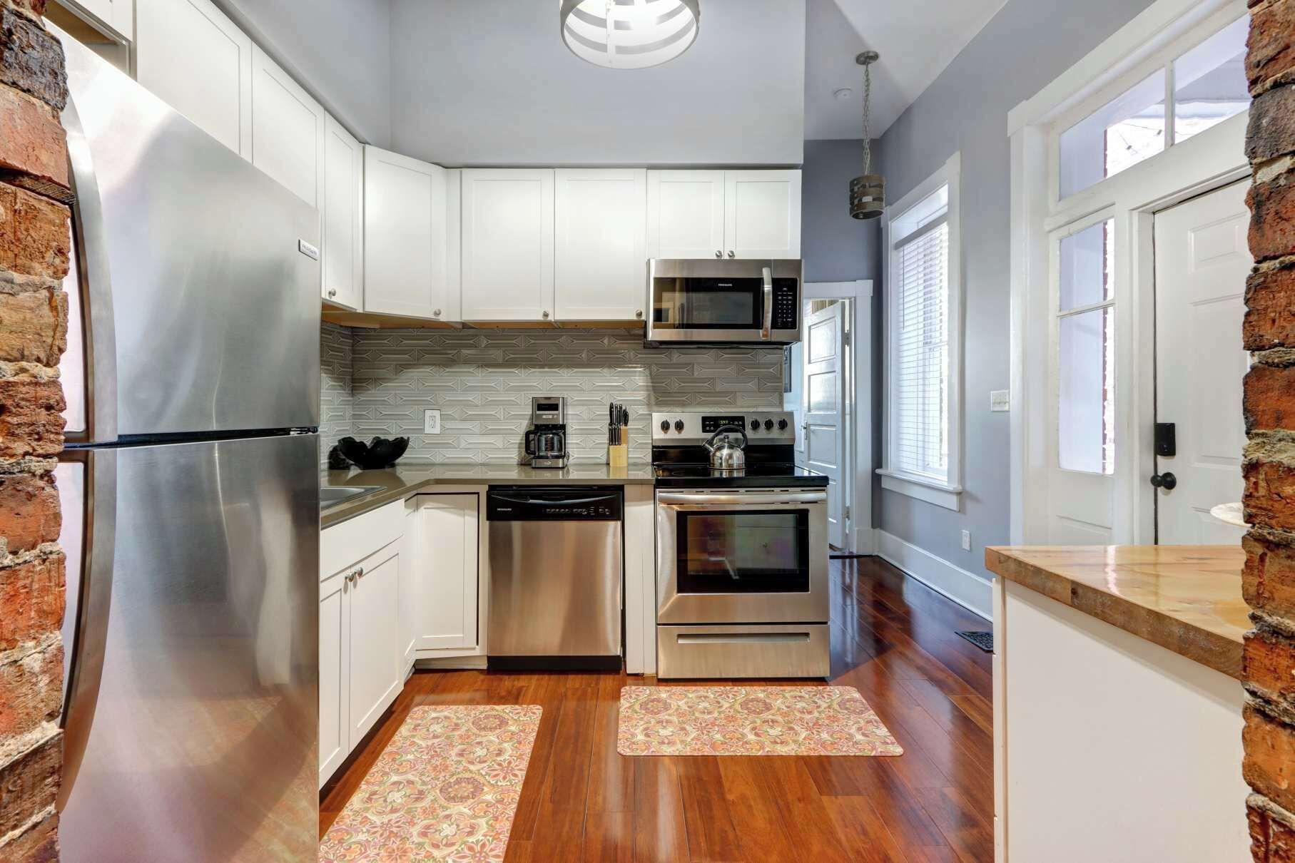 Una cocina moderna con electrodomésticos de acero inoxidable, armarios blancos y una pared de ladrillo decorativa.