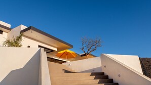 A modern staircase leading to a building with a yellow umbrella, a tree, and a clear blue sky. - Villa Damiana by The Agency Baja (El Pescadero)