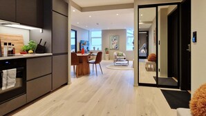 A modern kitchen with dark cabinets, a dining area with a round table, and a living space with a sofa and a coffee table. - Brand New & High-End, 3 Bedrooms 2 Bathrooms, Central Apartment (Bergen)