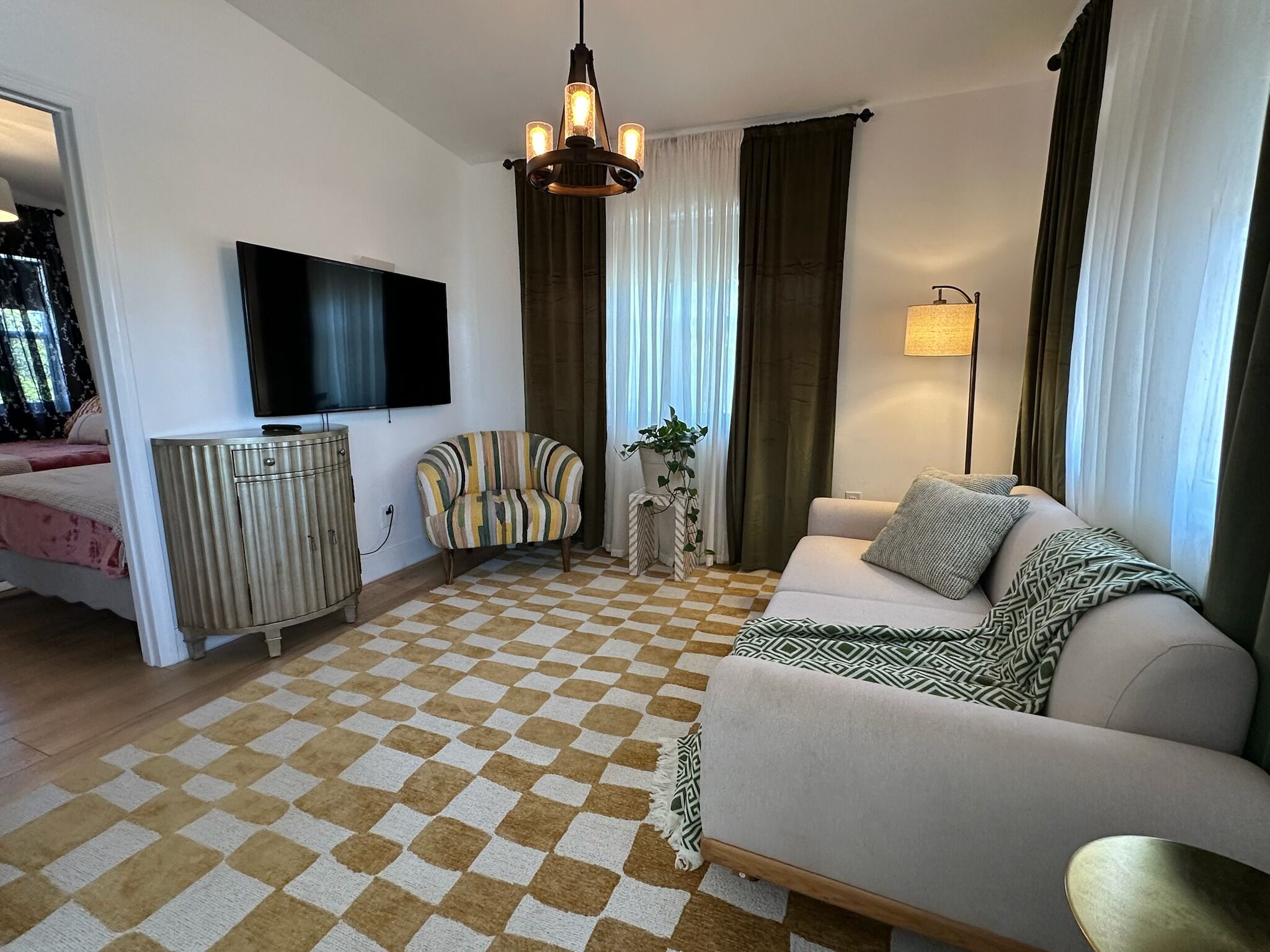 Een woonkamer met een geruite vloer, een bank, een televisie, een lamp en een gestreepte stoel.