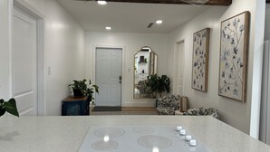 A modern kitchen with a central island, a hallway leading to a door, and two framed floral artworks on the walls. - Private duplex (second floor) centrally located to beaches and the city of Miami. (Miami)