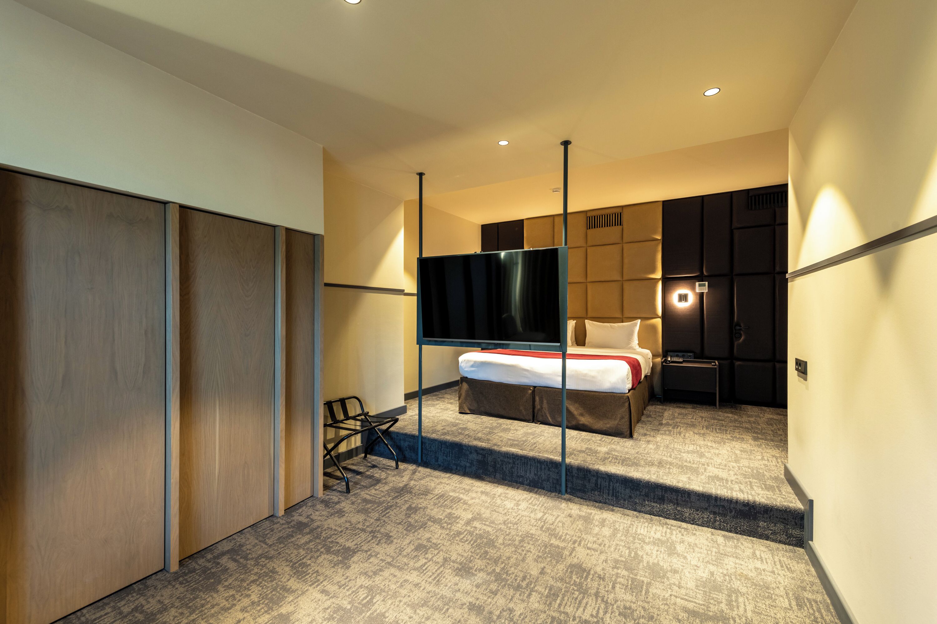 A modern hotel room with a bed, a TV, a desk, and a wardrobe.