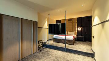 A modern hotel room with a bed, a TV, a desk, and a wardrobe.