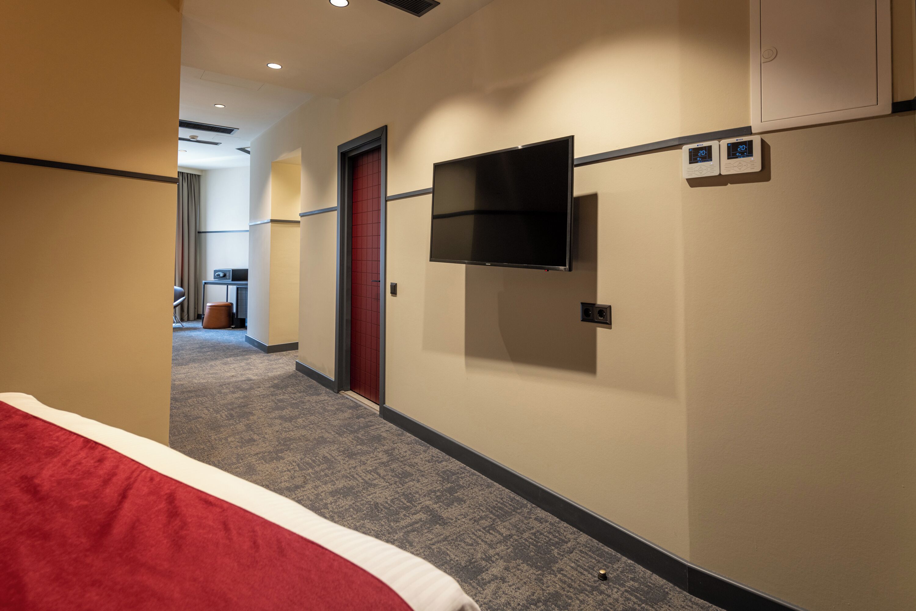 Una habitación de hotel con una cama, un televisor montado en la pared y un termostato.