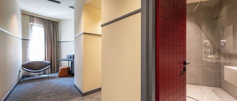 A hotel hallway with a shower area, a chair, and a small table.